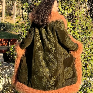 May include: A long, green velvet coat with a floral pattern and a fluffy, peach-colored fur trim. The coat has a hood and is lined with fur.