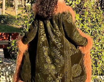 May include: A long, green velvet coat with a floral pattern and a fluffy, peach-colored fur trim. The coat has a hood and is lined with fur.
