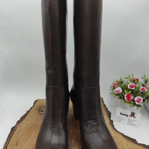 May include: A pair of brown leather knee-high boots with a rounded toe and a low block heel.