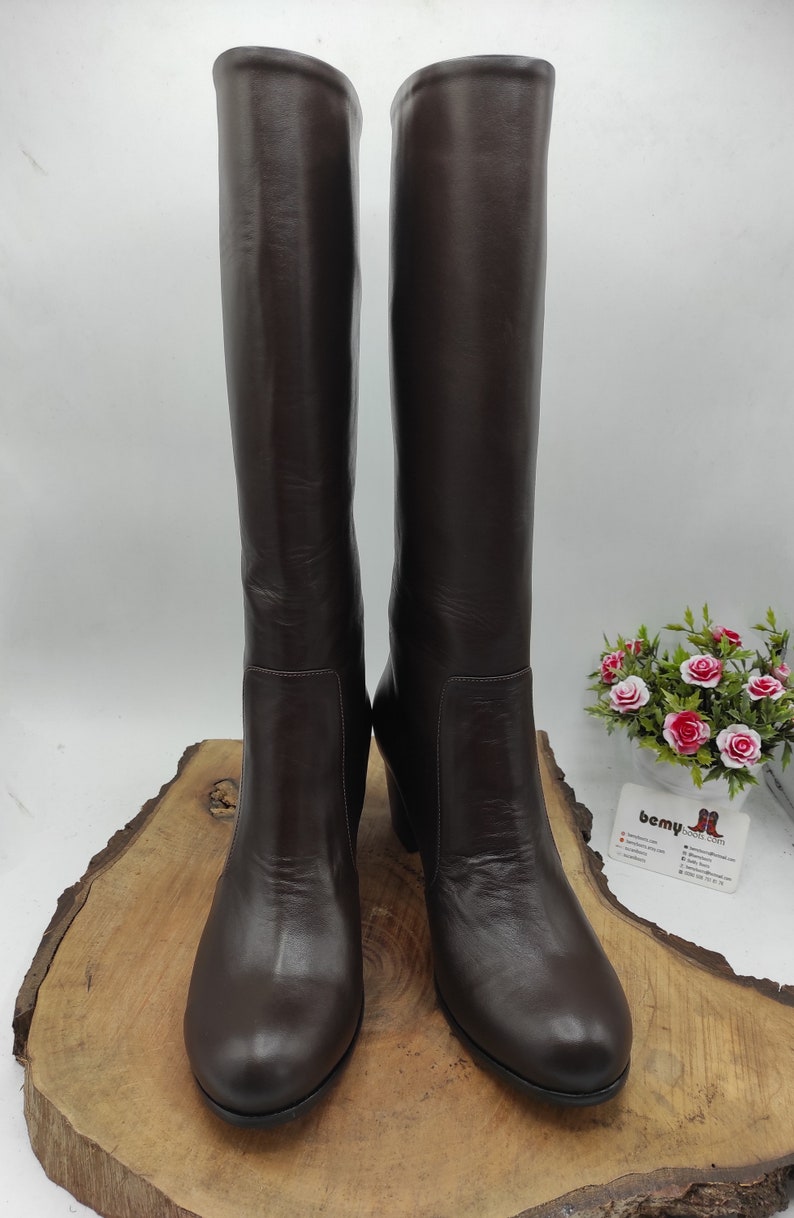 May include: A pair of brown leather knee-high boots with a rounded toe and a low block heel.