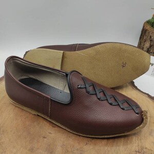 May include: A pair of brown leather slip-on shoes with a black braided design on the vamp. The shoes have a pointed toe and a flat sole. The size 37 is written on the sole of one shoe.