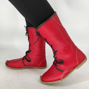 May include: Red leather boots with black laces and yellow stitching. The boots have a pointed toe and a flat sole.