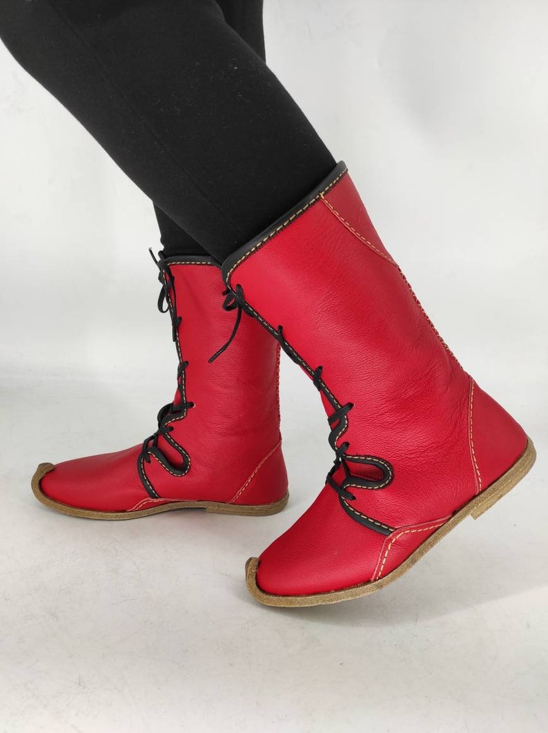 May include: Red leather boots with black laces and yellow stitching. The boots have a pointed toe and a flat sole.