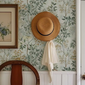 May include: A straw hat hangs on a hook against a wall with a green floral wallpaper. A wooden chair sits in front of the wall.