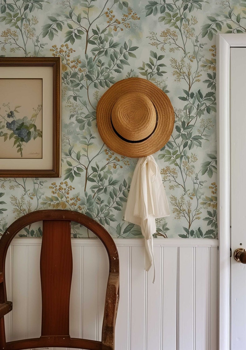 May include: A straw hat hangs on a hook against a wall with a green floral wallpaper. A wooden chair sits in front of the wall.