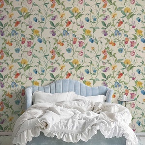 May include: A light blue upholstered bed with a scalloped headboard and white ruffled bedding, positioned against a cream-colored wallpaper featuring a repeating pattern of climbing vines with multi-colored sweet pea flowers in yellow, blue, and pink.