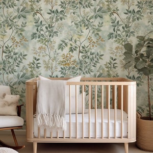 May include: A wooden crib with a white blanket and a white pillow. The crib is in front of a wall with a green and yellow floral wallpaper.