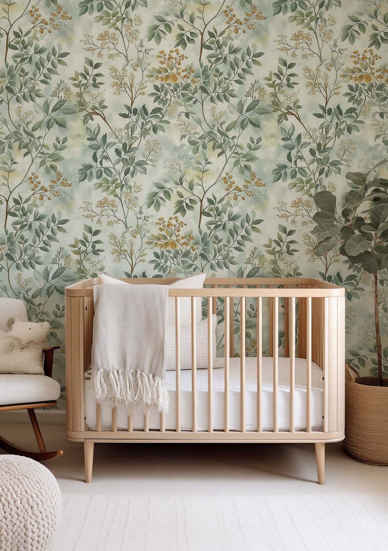 May include: A wooden crib with a white blanket and a white pillow. The crib is in front of a wall with a green and yellow floral wallpaper.