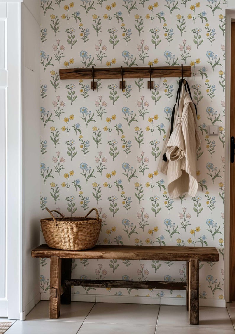 May include: A rustic wooden bench with a matching wall-mounted coat rack featuring four metal hooks. A woven wicker basket sits on the bench, and a light-colored jacket hangs from a hook. The wall is covered in white wallpaper with a floral pattern.