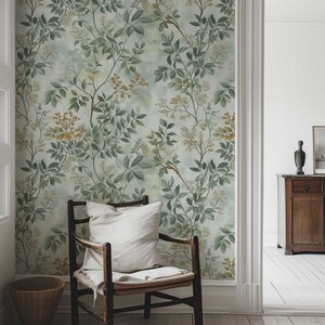 May include: A wooden chair with a white cushion sits in front of a wall covered in a green and yellow floral wallpaper. The wallpaper features a delicate pattern of leaves and flowers.