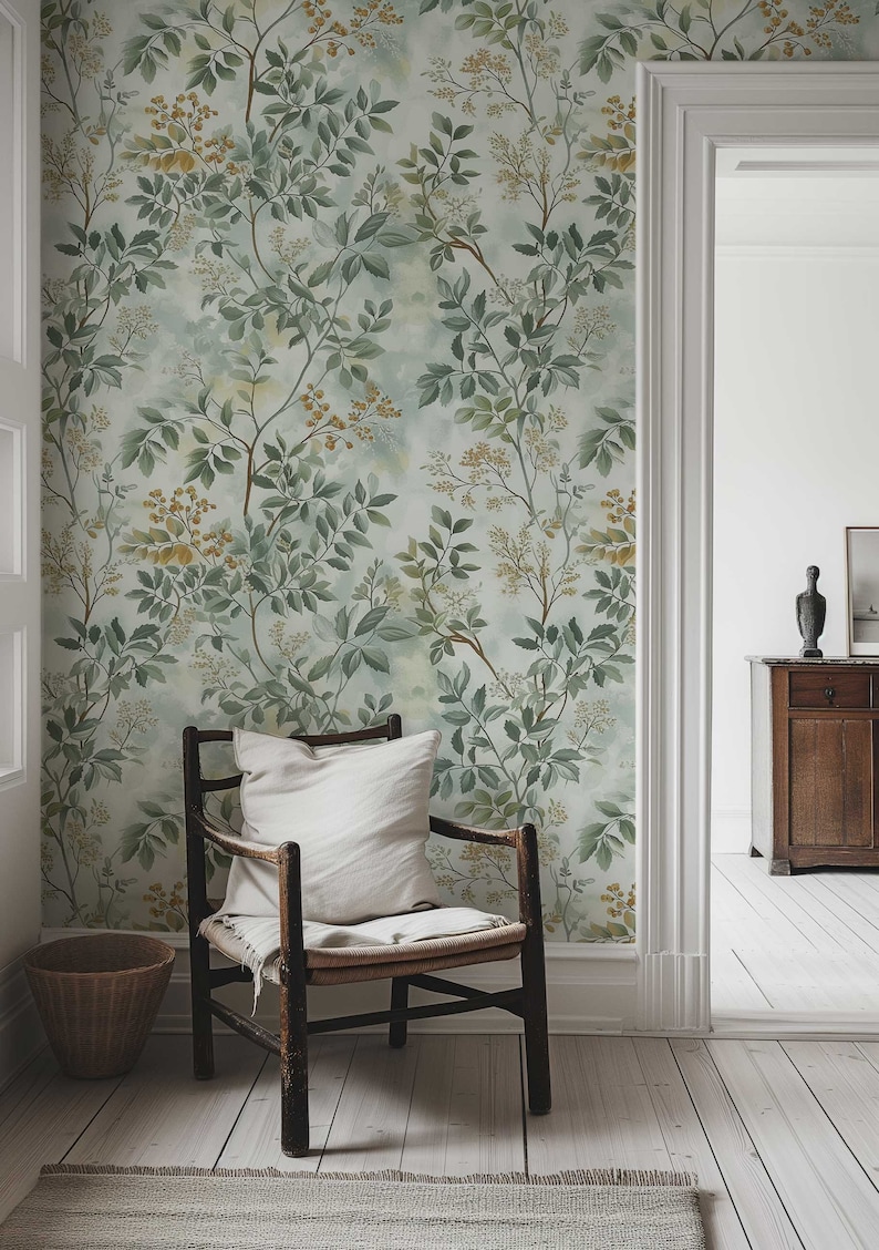 May include: A wooden chair with a white cushion sits in front of a wall covered in a green and yellow floral wallpaper. The wallpaper features a delicate pattern of leaves and flowers.