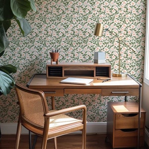 Puede incluir: Un escritorio de madera con un acabado de madera clara y una silla de ca&ntilde;a tejida. El escritorio tiene un caj&oacute;n y un estante. La pared detr&aacute;s del escritorio est&aacute; cubierta con papel tapiz floral con un patr&oacute;n rosa y verde.