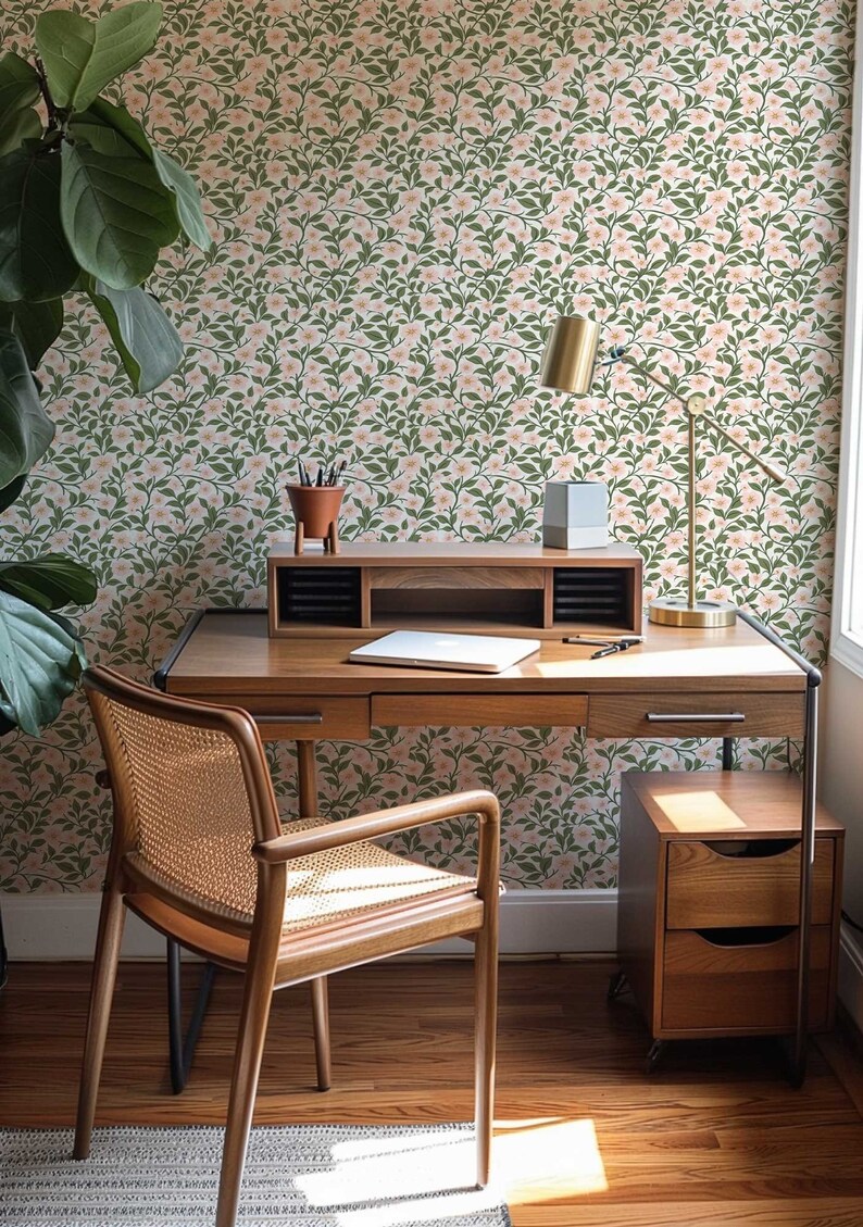 Puede incluir: Un escritorio de madera con un acabado de madera clara y una silla de ca&ntilde;a tejida. El escritorio tiene un caj&oacute;n y un estante. La pared detr&aacute;s del escritorio est&aacute; cubierta con papel tapiz floral con un patr&oacute;n rosa y verde.