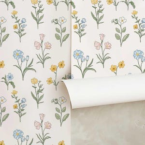 May include: Wallpaper featuring a repeating pattern of delicate wildflowers on a white background. The botanical illustrations include small blue, yellow, and pink flowers with green stems and leaves, arranged in a simple, spaced-out layout.
