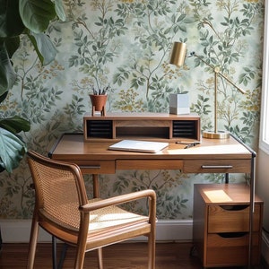 May include: A wooden desk with a woven chair, a lamp, and a small wooden file cabinet. The desk has a laptop and a potted plant on it. The wall behind the desk has a green and brown floral wallpaper.