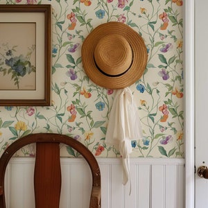 May include: A straw hat with a black ribbon band and a white fabric tie hanging from the brim, positioned on a wall covered in cream-colored wallpaper featuring a repeating pattern of colorful sweet pea flowers, green leaves, and thin vines.