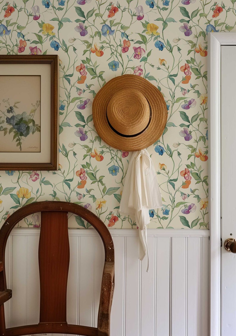 May include: A straw hat with a black ribbon band and a white fabric tie hanging from the brim, positioned on a wall covered in cream-colored wallpaper featuring a repeating pattern of colorful sweet pea flowers, green leaves, and thin vines.