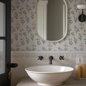 May include: A white vessel sink sits on a light-colored vanity with a wall-mounted faucet. Above the sink is an oval mirror against a wall covered in floral wallpaper featuring small yellow, blue, and pink flowers on a white background.