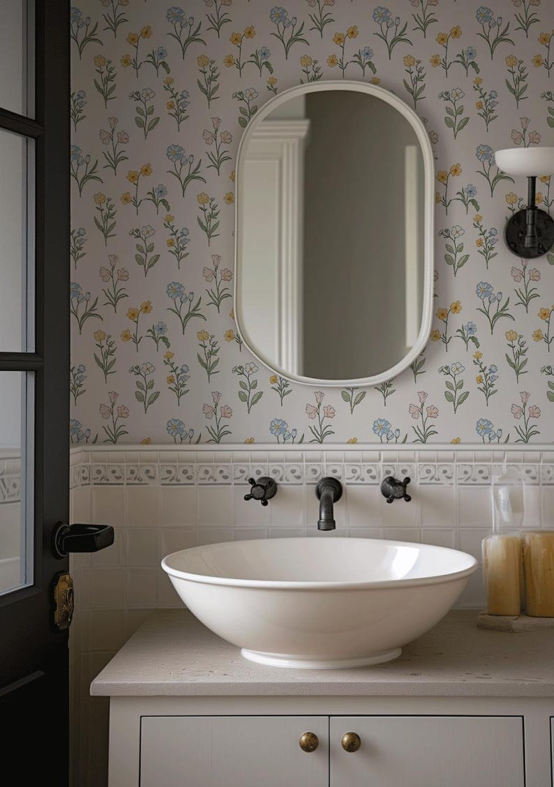 May include: A white vessel sink sits on a light-colored vanity with a wall-mounted faucet. Above the sink is an oval mirror against a wall covered in floral wallpaper featuring small yellow, blue, and pink flowers on a white background.