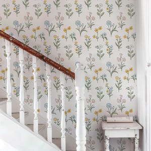 May include: Wallpaper featuring a repeating pattern of small, delicate flowers in shades of yellow, light blue, and soft pink with green stems and leaves on a white background, positioned behind a white staircase with a dark wood handrail.