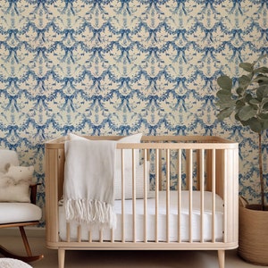 K&ouml;nnte beinhalten: Ein wei&szlig;es Babybett mit einer wei&szlig;en Decke und einem wei&szlig;en Kissen. Das Bett steht vor einer Wand mit einer blauen und wei&szlig;en floralen Tapetenmuster.