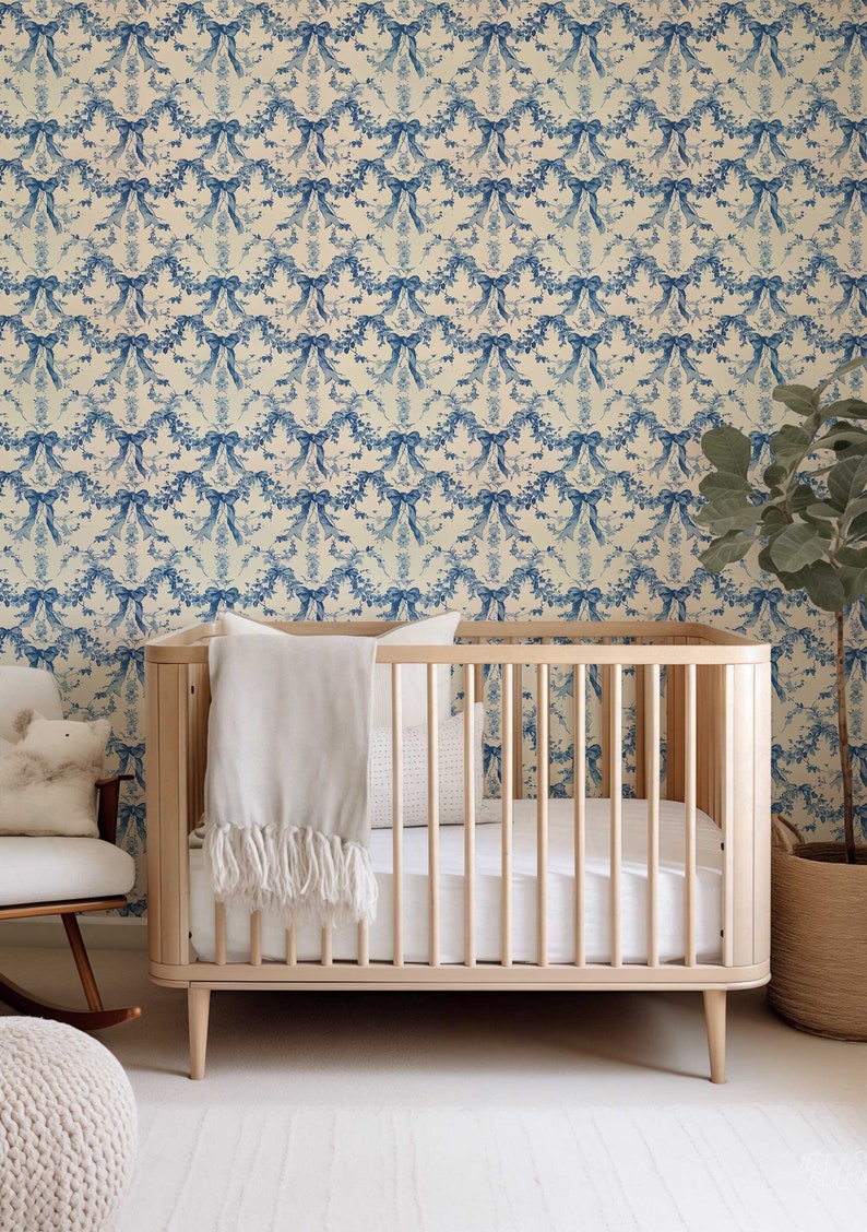 K&ouml;nnte beinhalten: Ein wei&szlig;es Babybett mit einer wei&szlig;en Decke und einem wei&szlig;en Kissen. Das Bett steht vor einer Wand mit einer blauen und wei&szlig;en floralen Tapetenmuster.
