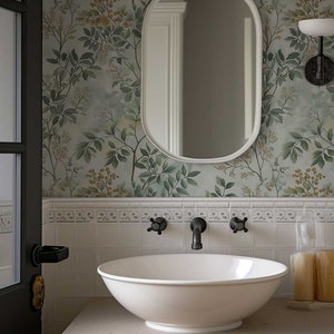 May include: A white porcelain sink with a white oval mirror above it. The sink is on a white countertop with a white cabinet underneath. The wall behind the sink is covered in a green and brown floral wallpaper.