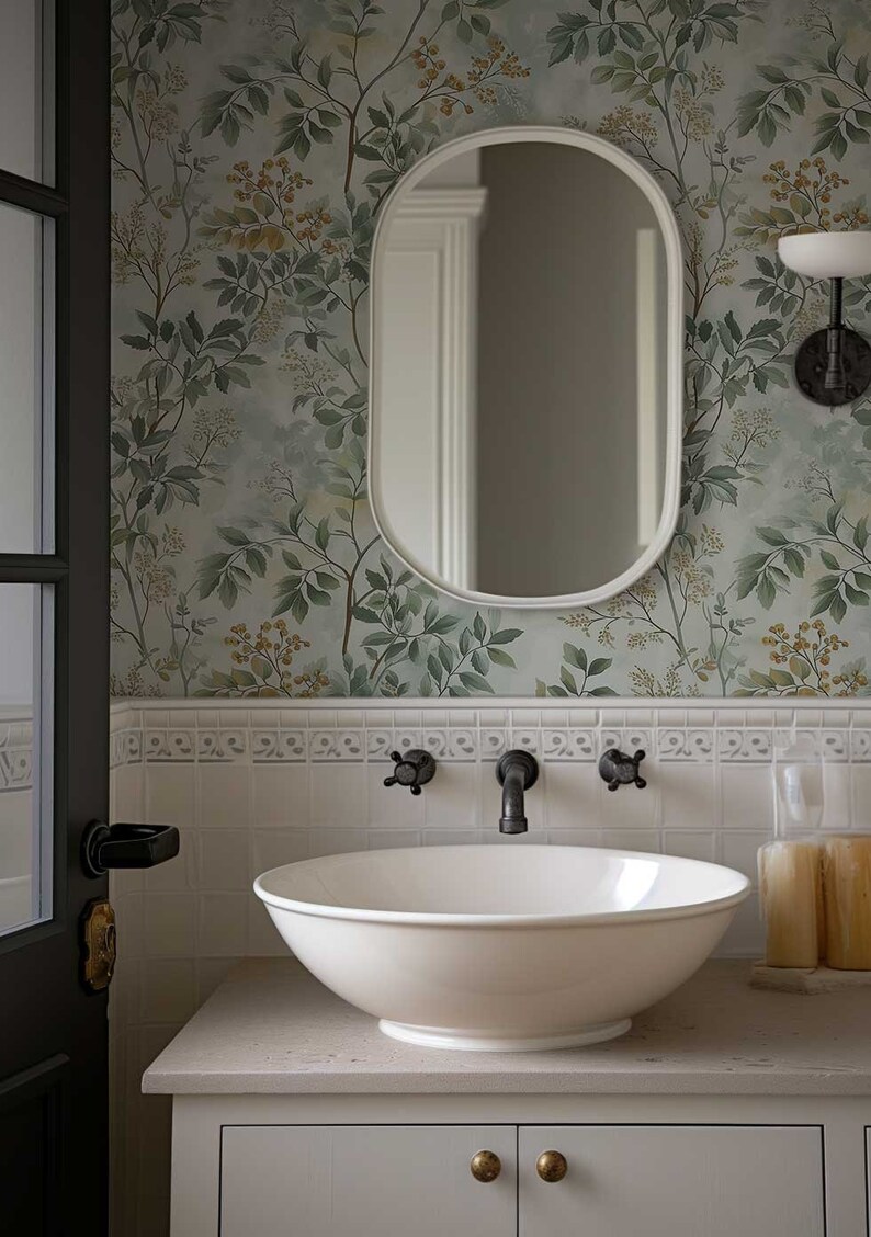May include: A white porcelain sink with a white oval mirror above it. The sink is on a white countertop with a white cabinet underneath. The wall behind the sink is covered in a green and brown floral wallpaper.