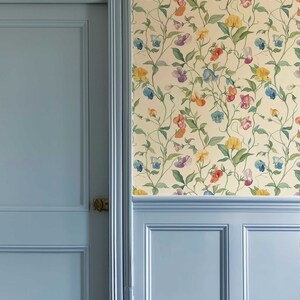 May include: A light blue paneled door and matching wainscoting are set against a cream-colored wall covered in wallpaper featuring a repeating pattern of climbing vines with green leaves and multi-colored sweet pea flowers in yellow, blue, and pink.