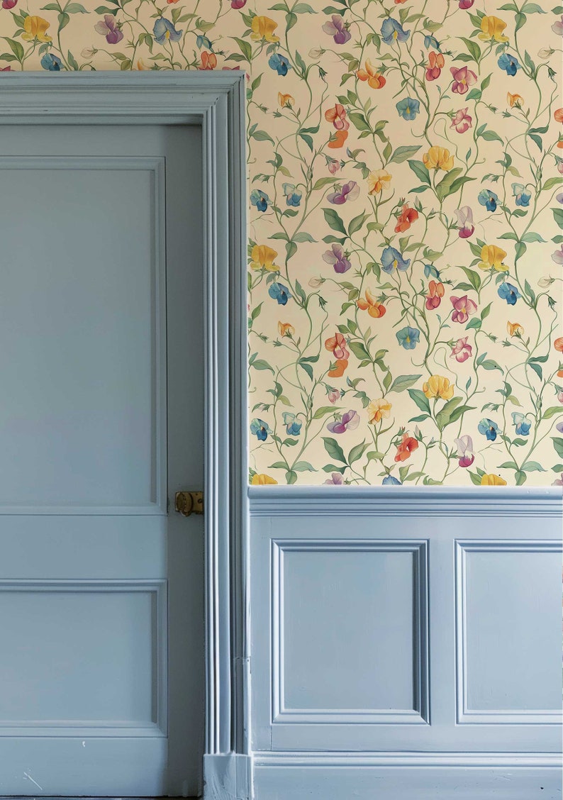 May include: A light blue paneled door and matching wainscoting are set against a cream-colored wall covered in wallpaper featuring a repeating pattern of climbing vines with green leaves and multi-colored sweet pea flowers in yellow, blue, and pink.