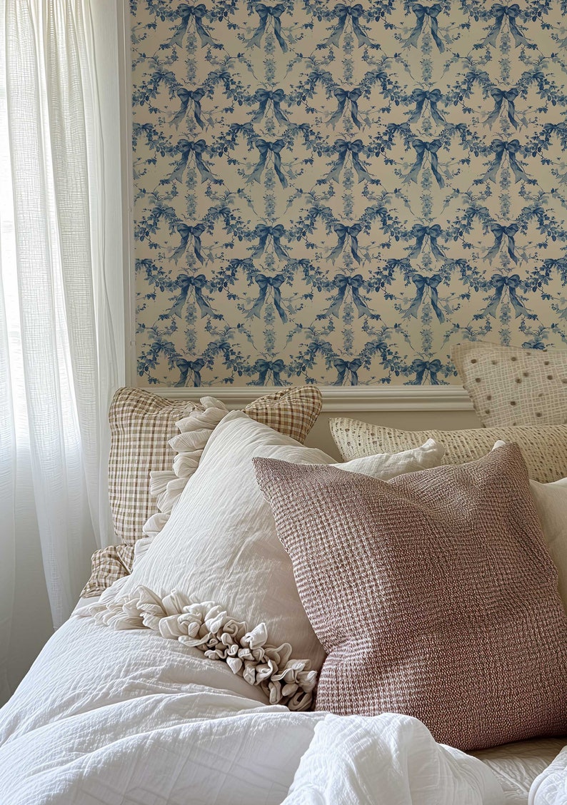 K&ouml;nnte beinhalten: Ein wei&szlig;es Bett mit einem wei&szlig;en Bettbezug und mehreren Kissen. Die Kissen sind in Wei&szlig;, Beige und Braun gehalten. Das Bett steht an einer Wand mit einer blauen und wei&szlig;en Blumen-Tapete.