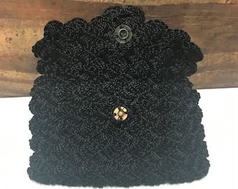 May include: Black, vintage-style handbag with a scalloped edge and a textured, woven appearance. The bag features a snap closure with a brass-colored button. The open flap reveals the interior of the bag.