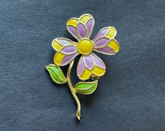 May include: A gold-tone metal brooch shaped like a flower with four petals. The petals are filled with lavender and yellow enamel. The center of the flower is a solid yellow circle. A curved gold stem features two bright green enamel leaves.