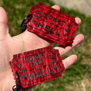 May include: Two red ticket-shaped keychains with black text. The top keychain says "Ticket to Hell" and the bottom keychain says "Admit One to Hell".