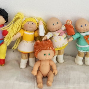 May include: A collection of nine Cabbage Patch Kids dolls, each with unique clothing and accessories. The dolls are made of plastic and have a variety of hairstyles and facial expressions.