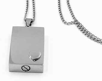 May include: A silver chain necklace with a rectangular pendant. The pendant has a small circle on the front and a screw on the side.