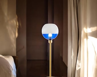 May include: A gold floor lamp with a round, blue and white glass shade. The lamp is on a light brown carpet.
