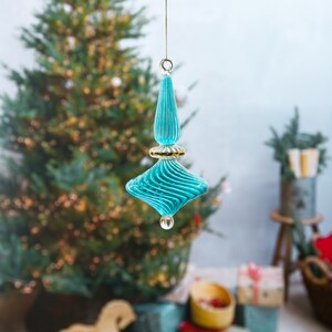 Puede incluir: Un adorno navide&ntilde;o de vidrio azul turquesa con ribete dorado y dise&ntilde;o en espiral. El adorno est&aacute; colgado de una cuerda.