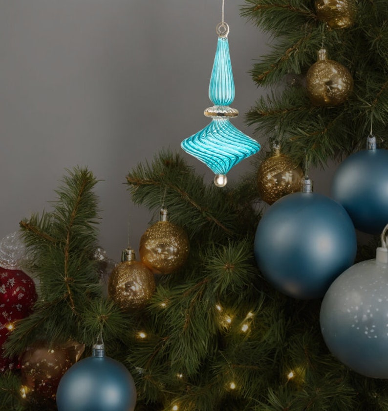 Puede incluir: Un adorno de Navidad de vidrio azul con un dise&ntilde;o de espiral cuelga de un &aacute;rbol de Navidad con otros adornos, incluidos adornos dorados y azules.