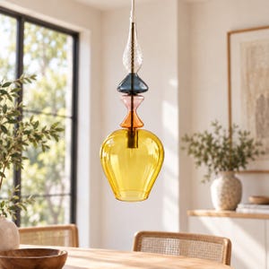 May include: A multi-colored glass pendant light fixture featuring a stack of distinct shapes. The top section is clear with a textured pattern, followed by a dark blue disc, a pink hourglass shape, an orange piece, and a large yellow base.