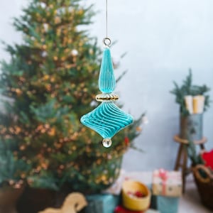Puede incluir: Un adorno navide&ntilde;o de vidrio azul turquesa con ribete dorado y dise&ntilde;o en espiral. El adorno est&aacute; colgado de una cuerda.