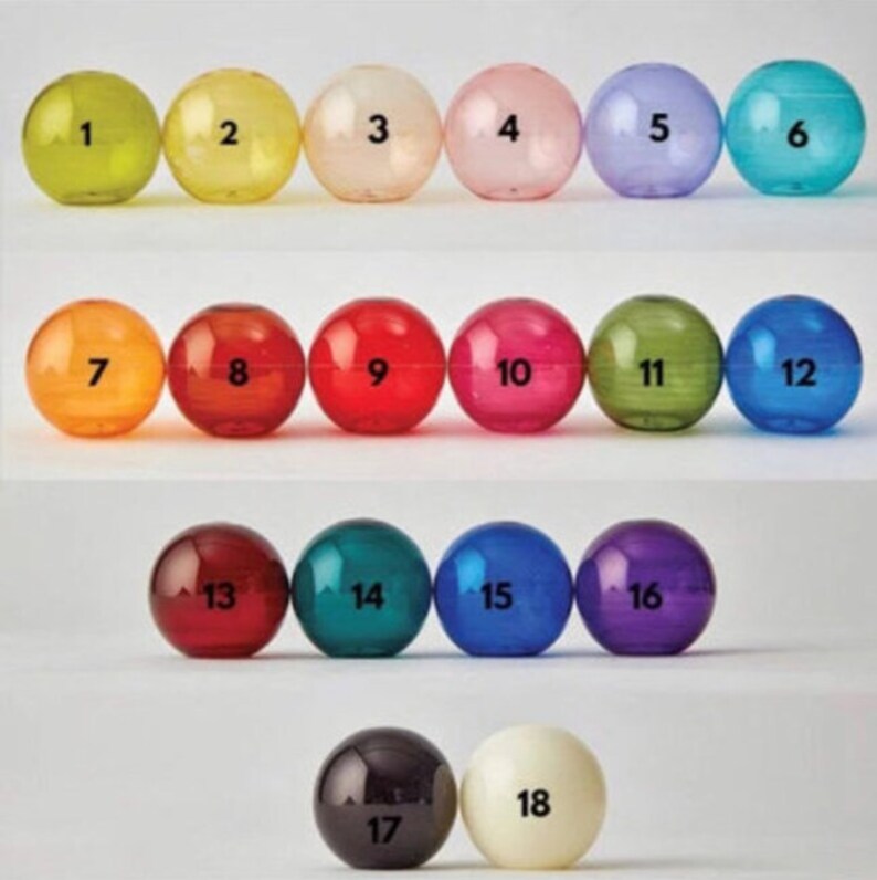 Puede incluir: Dieciocho bolas de vidrio de colores numeradas del 1 al 18. Las bolas est&aacute;n dispuestas en tres filas de seis, siendo la primera fila amarilla, verde, blanca, rosa, morada y azul. La segunda fila es naranja, roja, roja, rosa, verde y azul. La tercera fila es roja, verde, azul, morada, negra y blanca.