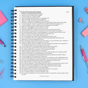 May include: A spiral bound notebook with a white cover and black text that reads "Trauma Processing Prompts". The notebook is open to a page with a list of 42 questions about trauma processing.