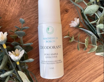 Könnte beinhalten: Ein weißer Deodorant-Stick mit dem Text "Magnesium Boron Deodorant" und "Pure Simple Effective". Das Produkt ist 85g und ist von weißen Blumen und grünen Blättern umgeben.