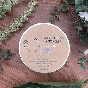 以下が含まれることがあります： 「All Natural Lotion Bar」と「Lavender」の文字が入った、丸い茶色と白のラベンダーローションバーのラベル。 ココナッツオイルやシアバターなどの成分が記載されています。 正味重量は85g。 木製の表面に、装飾的な緑の葉が周りにあります。