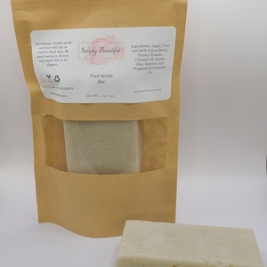 May include: A brown paper bag with a white label that says "Simply Beautiful" and "Foot Scrub Bar". The label also lists the ingredients: Sugar, Pour and Melt, Cocoa Butter, Pumice Powder, Coconut Oil, Kaolin Clay, Beeswax and Peppermint Essential Oil. The bag contains a white foot scrub bar.