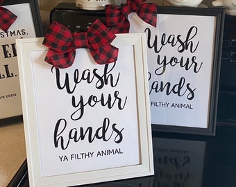 Puede incluir: Dos carteles enmarcados en blanco con texto negro que dice "Wash your hands Ya Filthy Animal" y "Wash your hands Filthy Animal". Cada cartel tiene un lazo de cuadros rojos y negros en la parte superior.