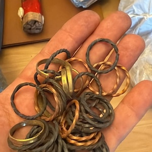 Puede incluir: Una mano sosteniendo un montón de anillos de metal de diferentes tipos. Los anillos son de cobre, latón y plata. Algunos de los anillos están retorcidos o trenzados.