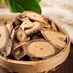 May include: Close-up of a round, woven basket filled with dried, light brown, sliced roots. The roots have a textured surface and varying shapes. A green leaf is visible in the background.