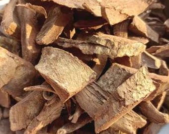 May include: Close-up of a pile of light brown, irregularly shaped wood chips. The chips vary in size and texture, with some appearing rough and others smoother. The lighting highlights the natural grain and color variations of the wood.